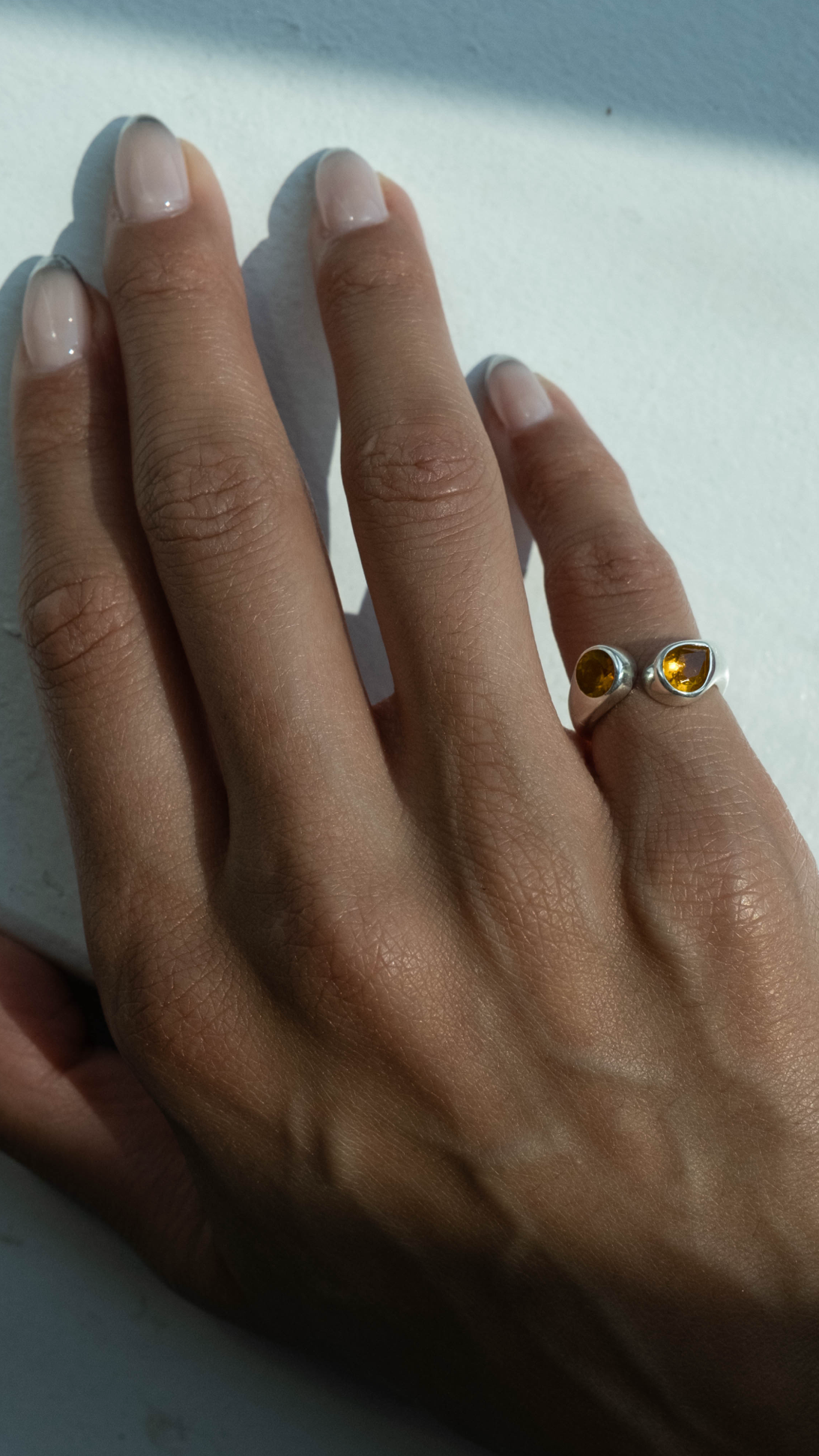 A close-up of a hand resting on a white surface, wearing a gold ring with two small oval yellow gemstones.