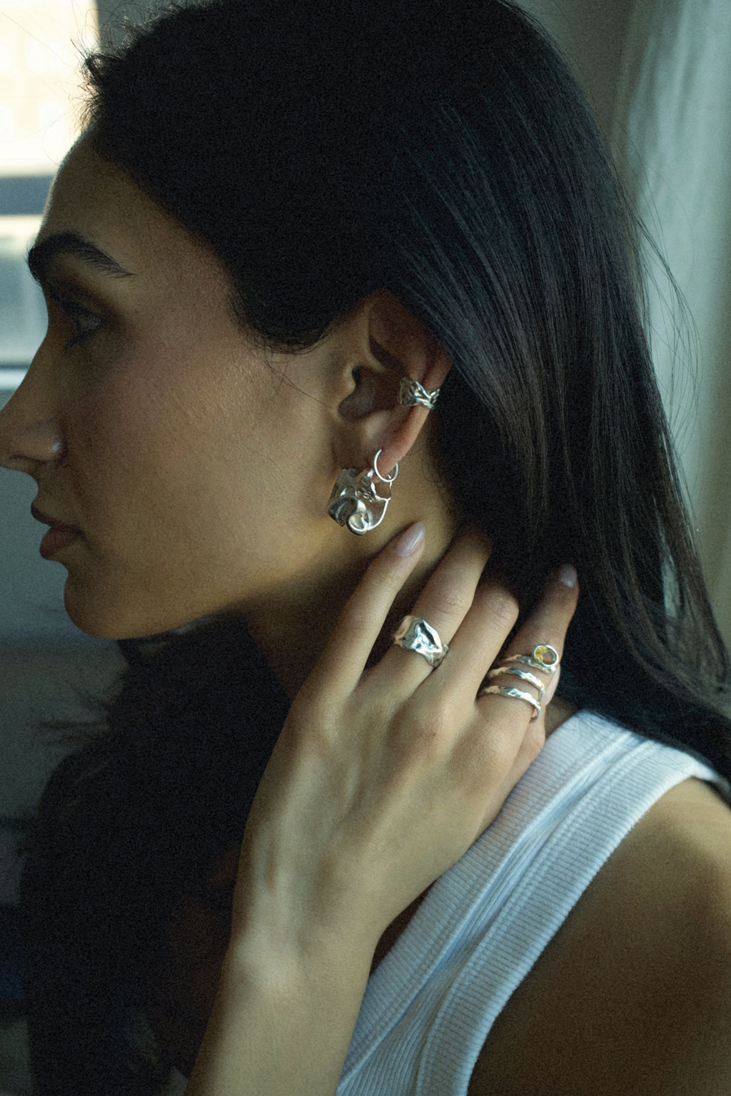Woman wearing silver earrings and rings, with a neutral background