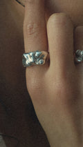 Close-up of a person wearing a silver bow-shaped ring on their finger.